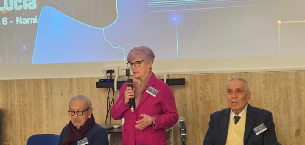 Immagine di una conferenza presso l'Asp Beata Lucia a Narni, con relatori tra cui una donna in giacca rosa che parla al microfono e due uomini seduti accanto a lei, sul tema dell'intelligenza artificiale in sanità.
