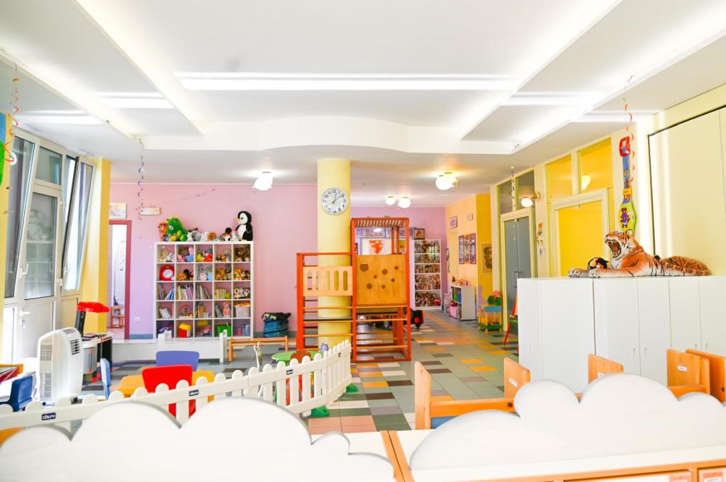 Interno di una scuola dell'infanzia con pareti colorate, mobili giocattolo e scaffali pieni di peluche e libri.