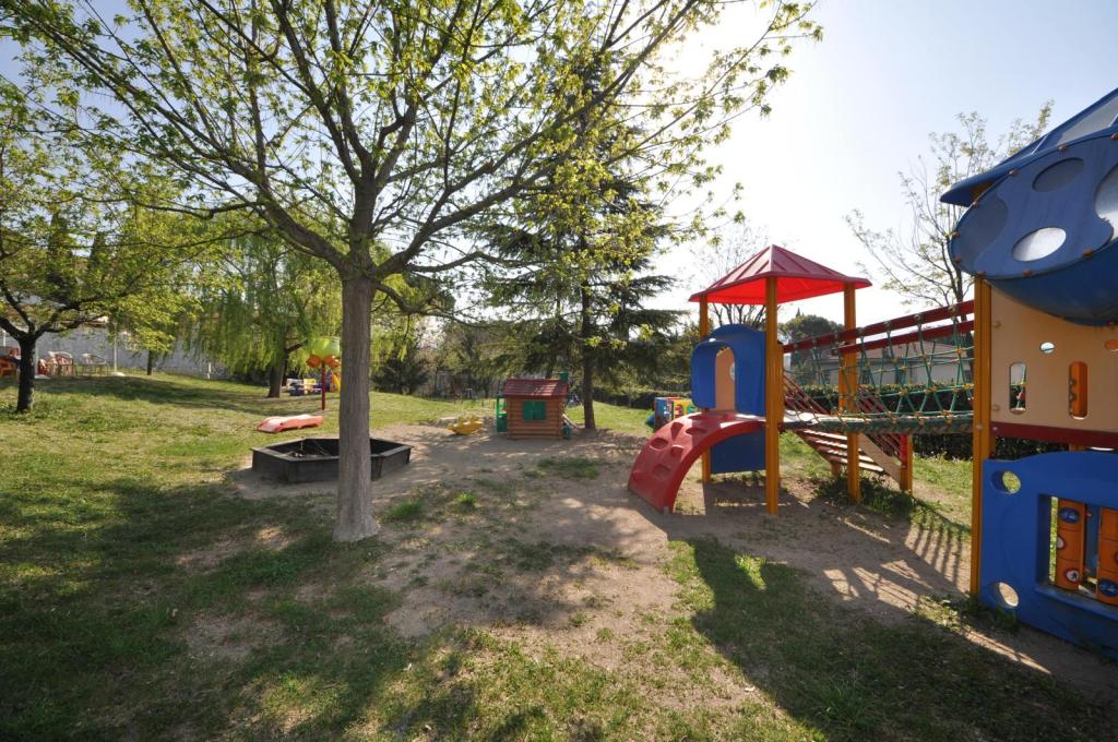 Area giochi all'aperto con attrezzature colorate, inclusi scivoli e una piccola casa, circondata da alberi in un ambiente verde.