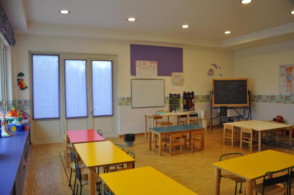 Aula di una scuola dell'infanzia con tavoli colorati e lavagna, dotata di finestre che offrono luce naturale.