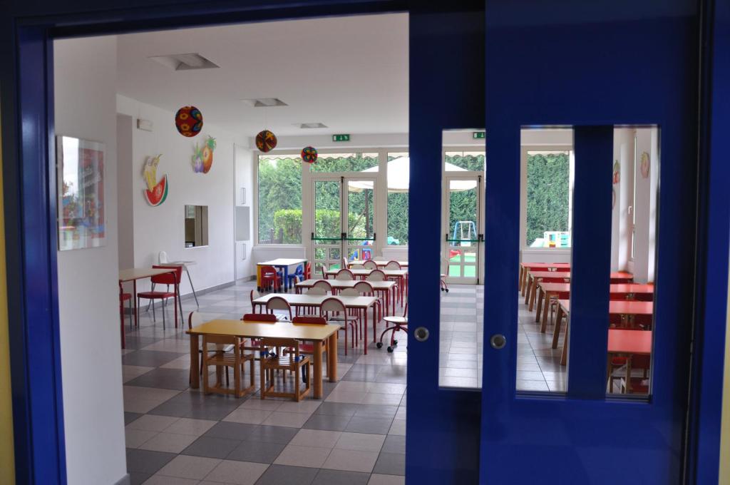 Interno di una sala per attività educative, con tavoli e sedie colorate per bambini, decorazioni murali e accesso a un giardino esterno.