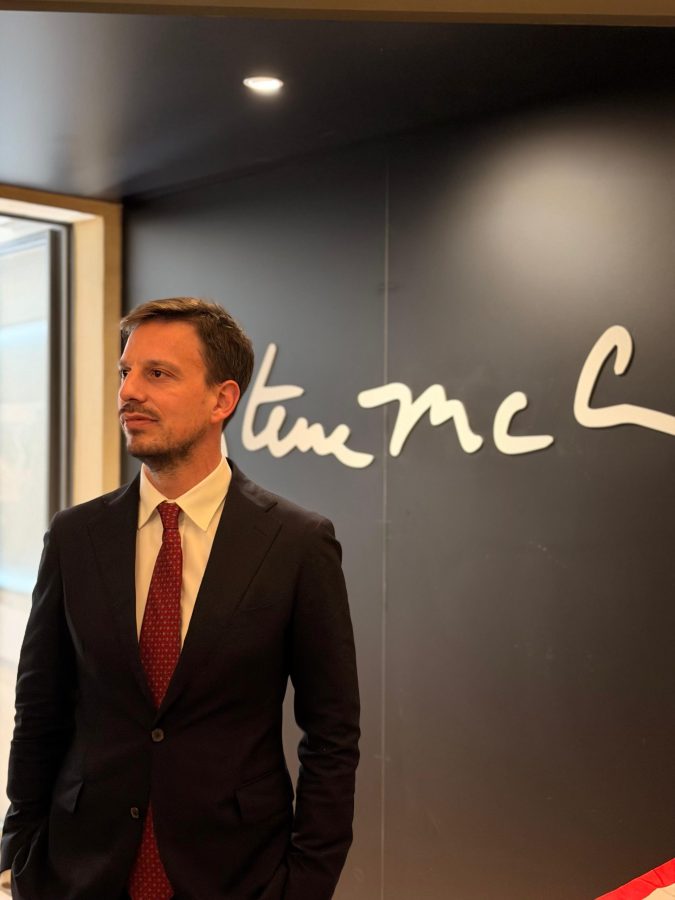 Un uomo in abito scuro con cravatta rossa in piedi di fronte a un muro con il nome 'Steve McCurry' scritto in bianco.