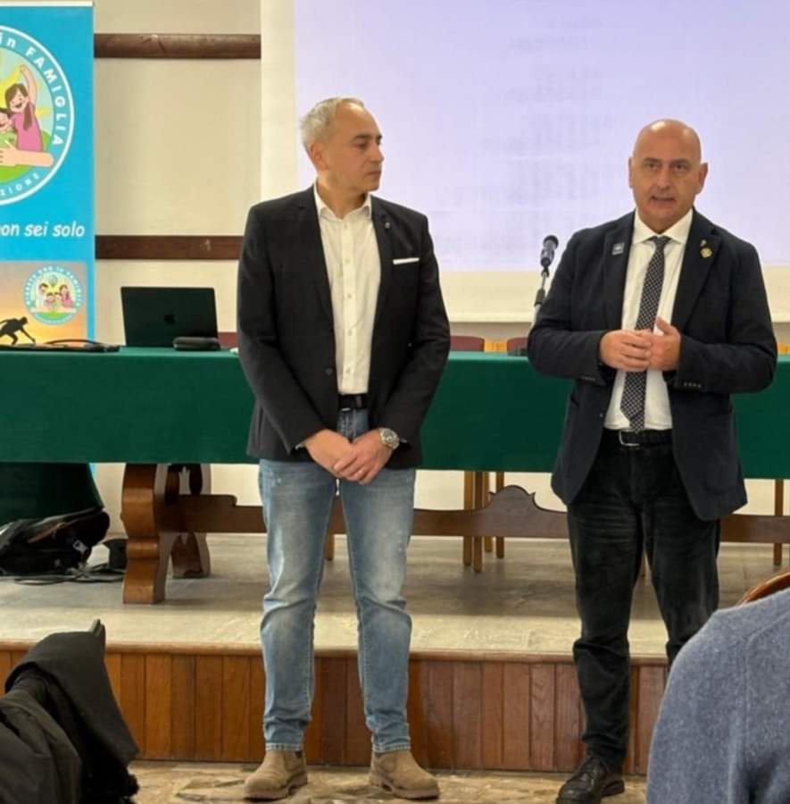 Due relatori parlano durante un incontro sulla gestione del diabete di tipo 1, con un tavolo verde sullo sfondo e un banner colorato di un'associazione.