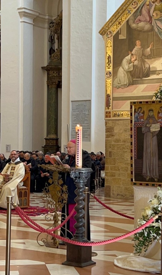 Un momento solenne durante la celebrazione nella Basilica di Santa Maria degli Angeli, con un vescovo che guida la Liturgia della Luce e un cero pasquale acceso in primo piano, mentre il pubblico assiste in adorazione.