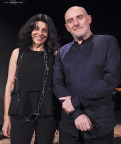 Two people posing for a photo, one wearing a black top and the other wearing a dark shirt, both smiling.