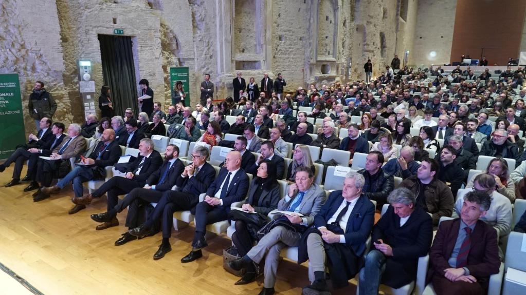 A large audience seated in a spacious venue, attentively listening during a presentation or event.