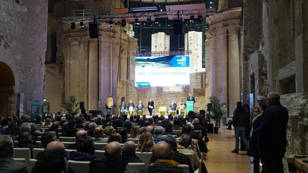 A conference taking place in a historic venue, featuring a panel of speakers at the front, with an audience seated in rows facing them.