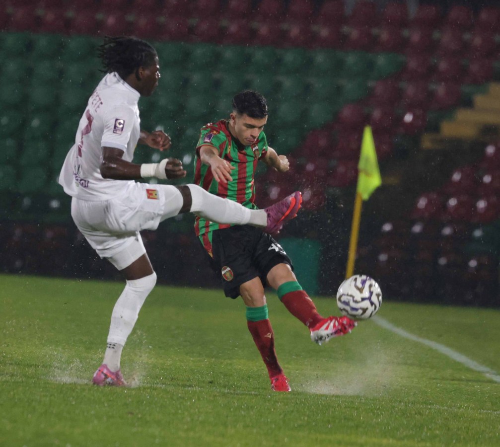 Giocatore della Ternana in maglia verde e rossa che tenta di calciare il pallone mentre un avversario del Livorno, in maglia bianca, sta cercando di fermarlo. La scena si svolge in un campo bagnato dalla pioggia.