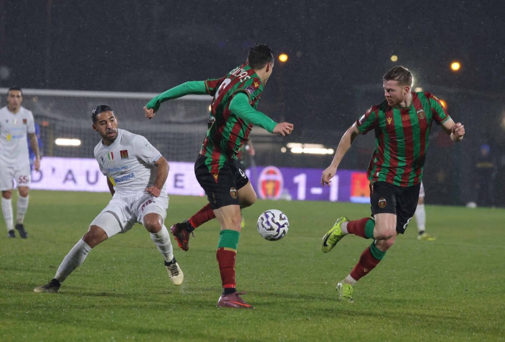 Giocatori della Ternana in azione durante una partita di calcio sotto la pioggia, con intensi contrasti tra le squadre in divise colorate.
