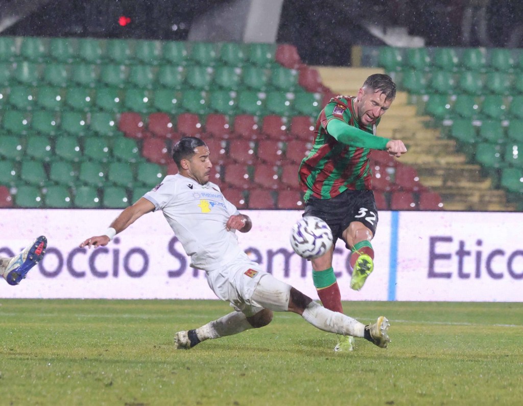 Un giocatore della Ternana calcia verso la porta mentre un avversario del Livorno tenta di intervenire, in una partita di calcio sotto la pioggia.