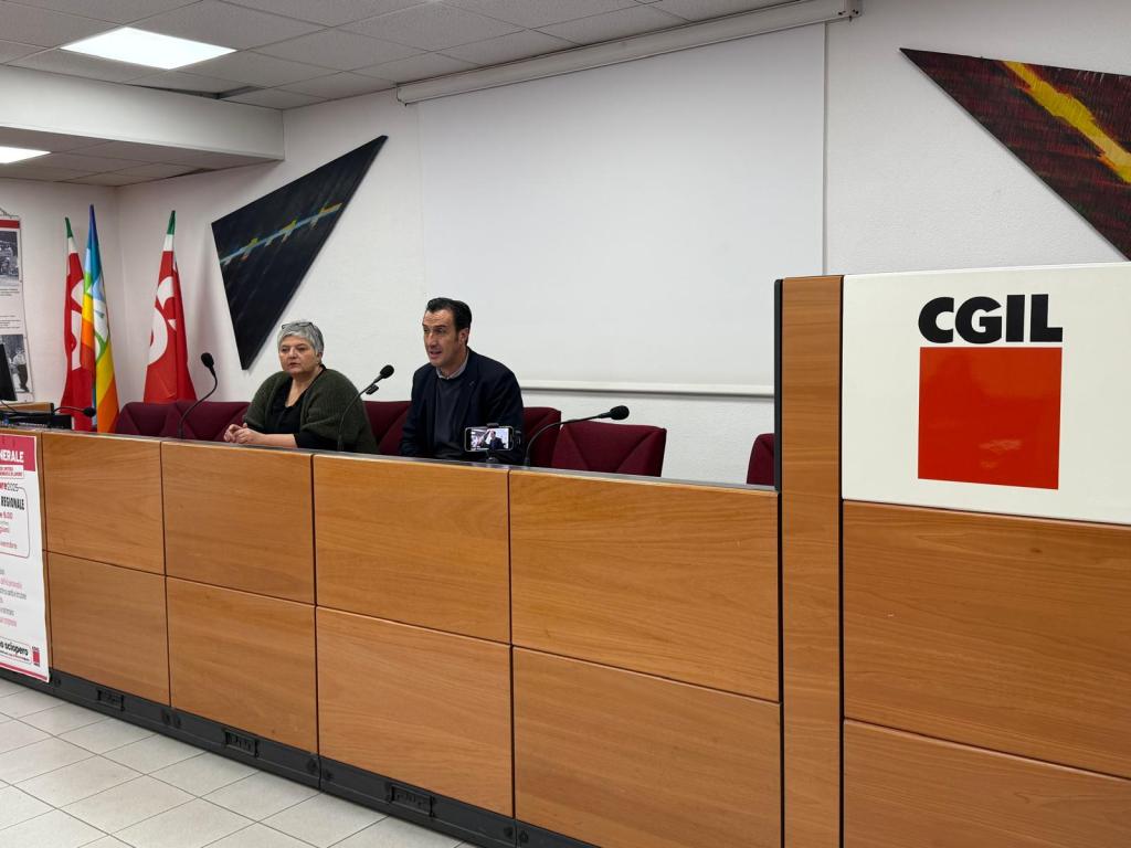 Conferenza stampa della CGIL a Terni con due relatori seduti a una scrivania in legno, tra bandiere e un cartello con il logo CGIL sul lato destro.