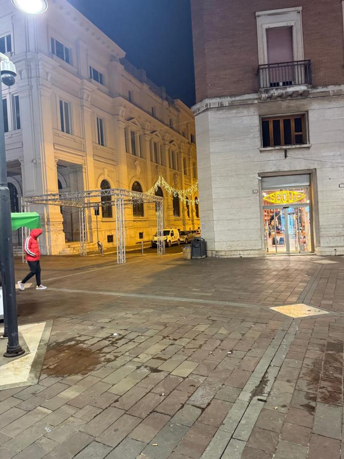 Vista notturna di una strada con un edificio illuminato e una vetrina di negozio, con una persona che cammina in un abbigliamento rosso.