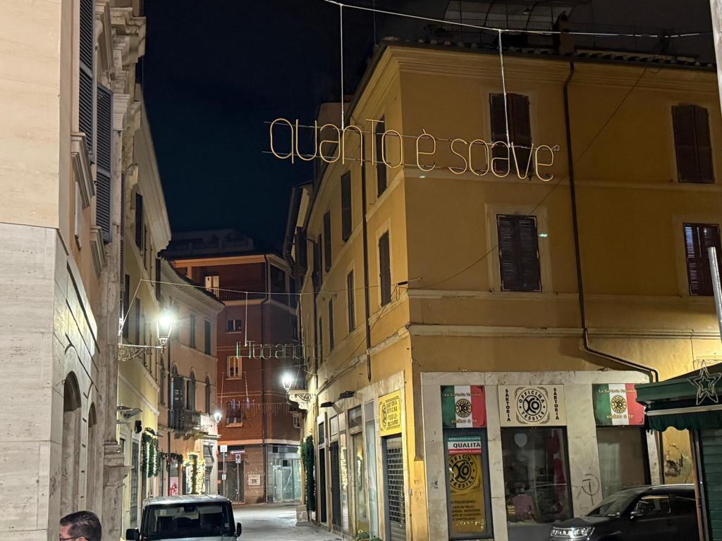 Una via illuminata di notte con insegne e luci decorative. Si vedono edifici colorati e un'atmosfera suggestiva.