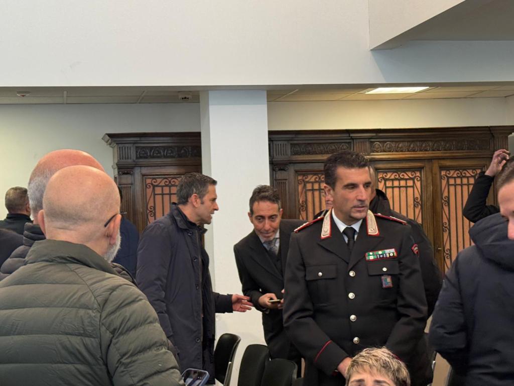 A group of people gathered in a room, including a uniformed officer and several men in casual attire, engaged in conversation.