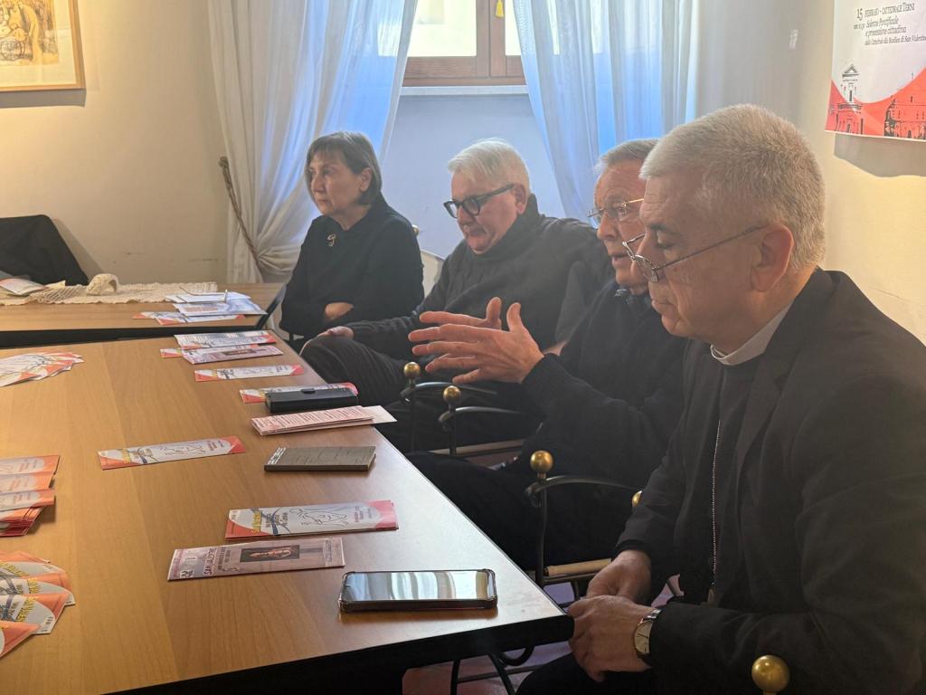 A group of four individuals seated at a table during a discussion. They appear engaged, with pamphlets and documents spread out in front of them.