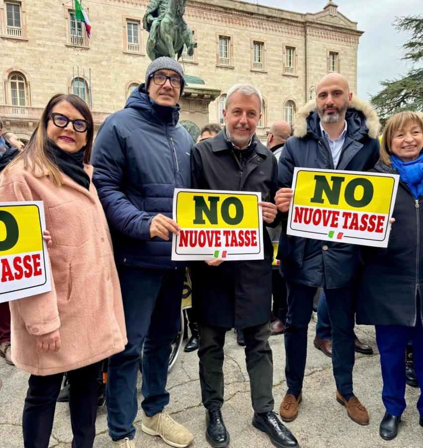A group of five people holding signs that read 'NO NUOVE TASSE' at a protest, with a historic building and a statue in the background.
