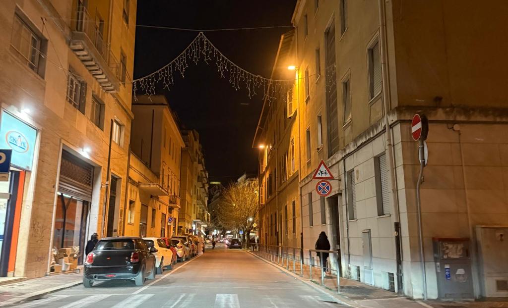 A nighttime street view showing illuminated buildings, parked cars, and decorative lights overhead.