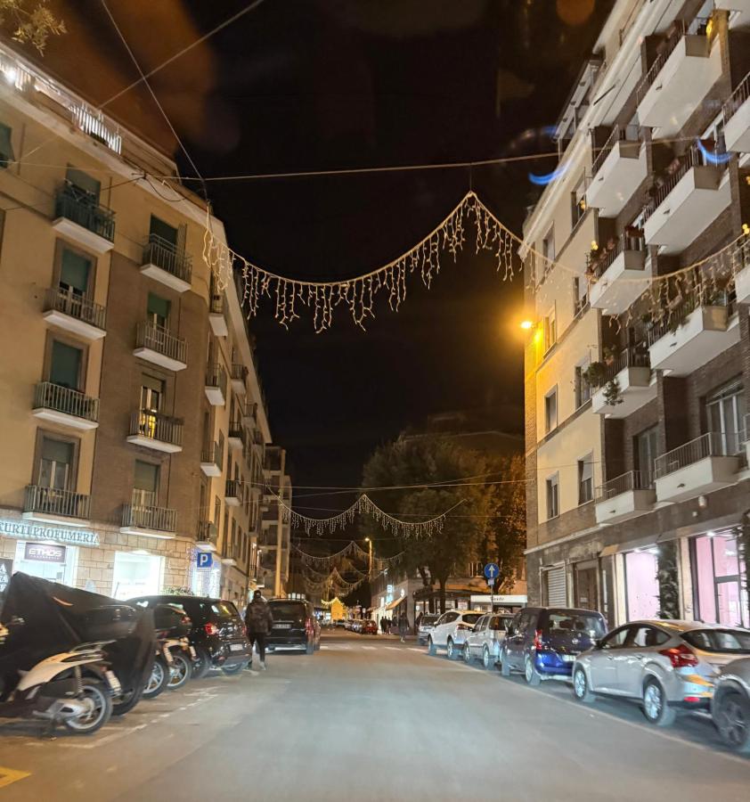 A night scene of a city street lined with parked cars, illuminated by streetlights and decorated with hanging lights overhead.