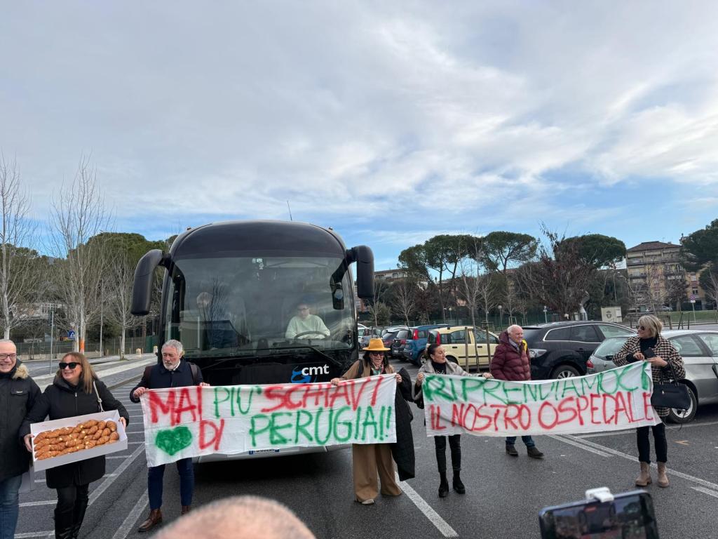 Protesters holding banners in front of a bus, advocating for their local hospital and expressing pride in Perugia.