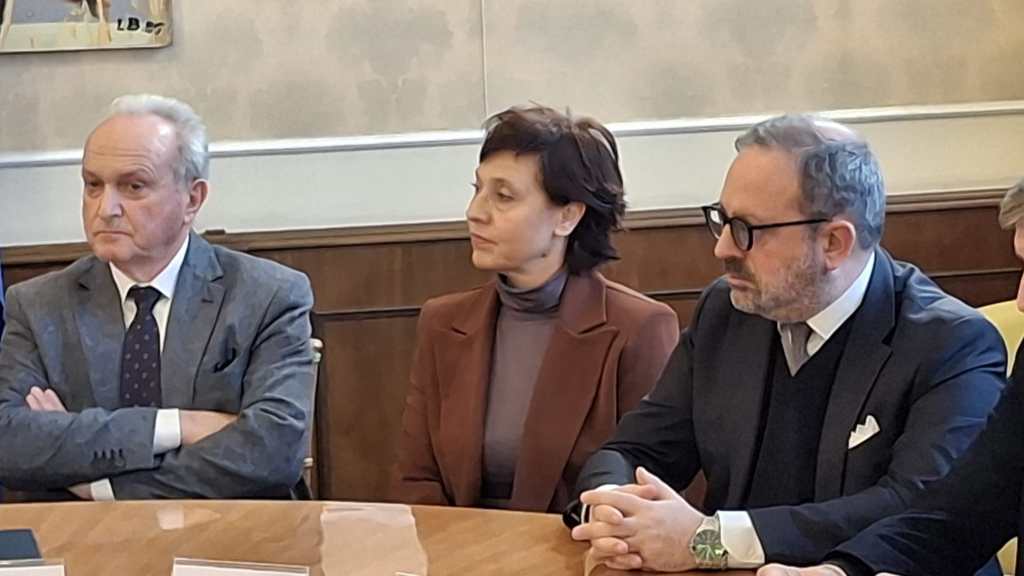 A group of three people seated at a table in a formal setting, engaged in a discussion or meeting.