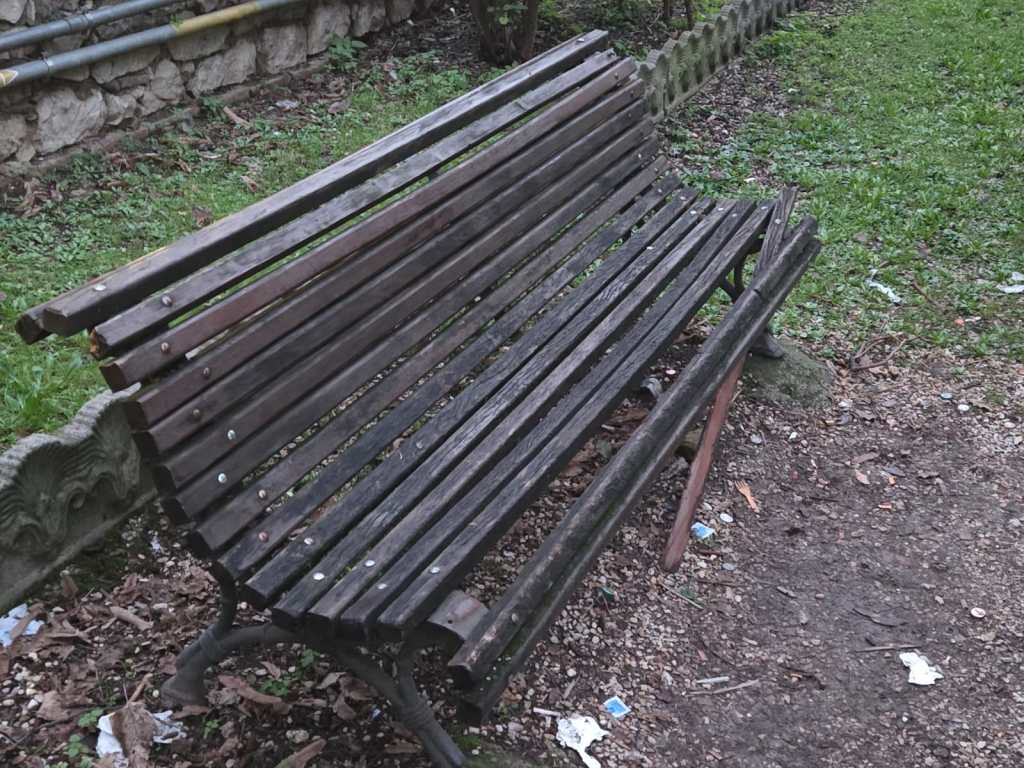 A weathered wooden park bench sitting on a grassy area with some debris around.