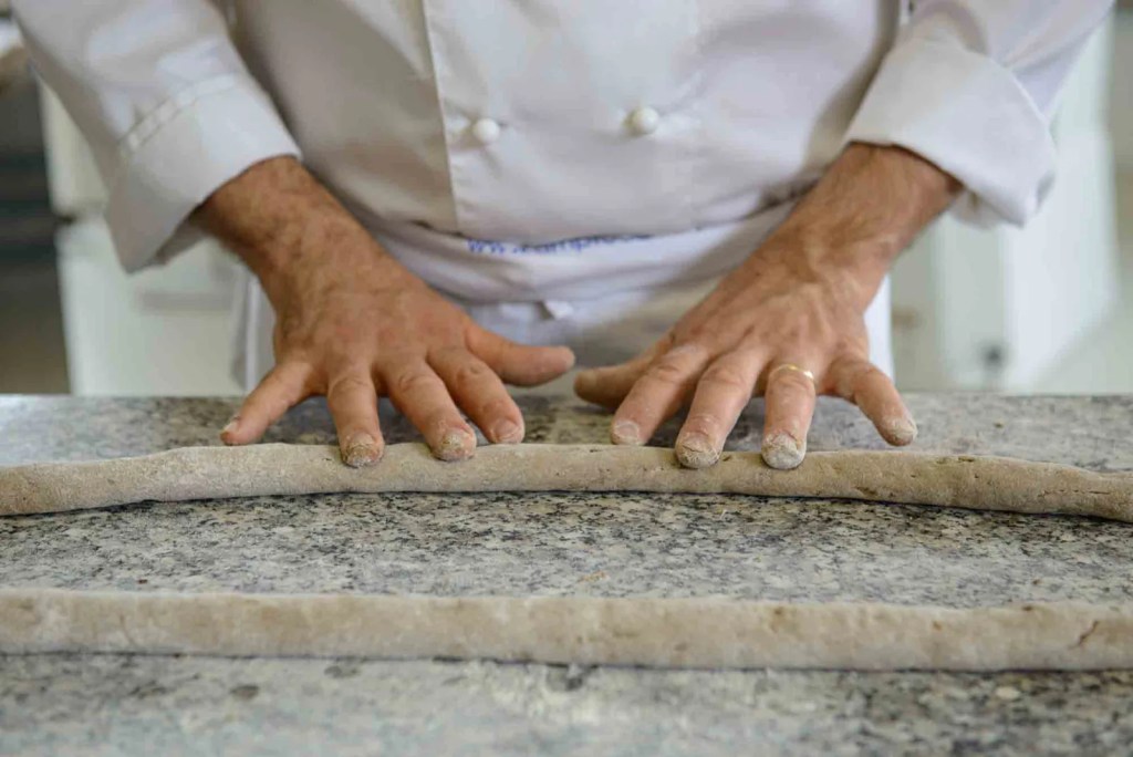 A chef's hands kneading and shaping dough on a granite countertop.