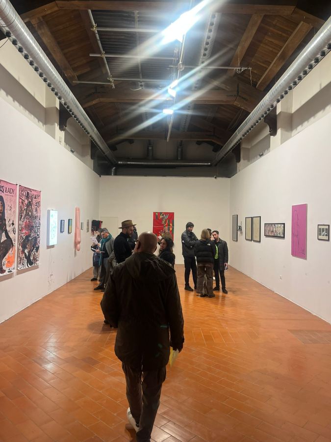 An art gallery with visitors exploring various artworks on the walls, featuring a mix of paintings and framed images, and bright ceiling lights illuminating the space.
