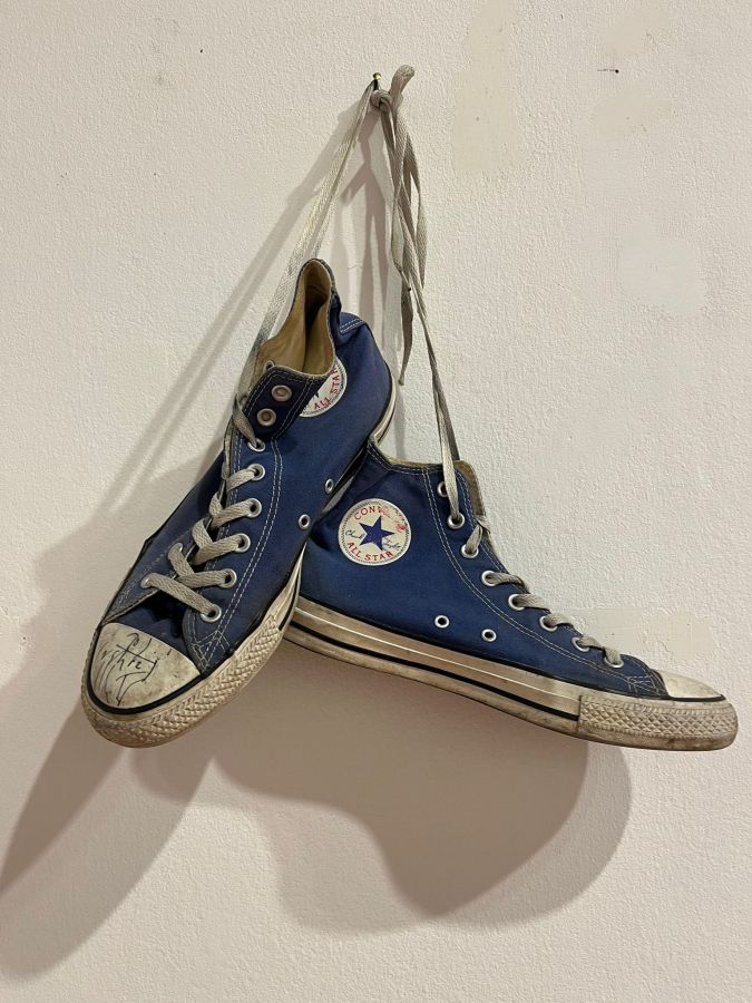 A pair of blue Converse All Star sneakers hanging by their laces on a wall.