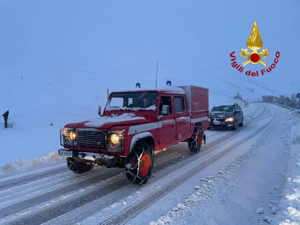 Un veicolo dei Vigili del Fuoco rosso in un paesaggio innevato, mentre un'auto passa su una strada coperta di neve.