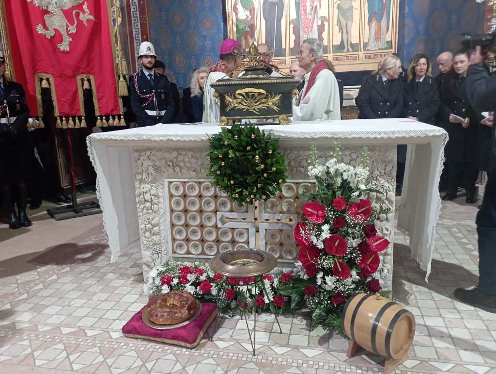 A ceremonial altar decorated with flowers and greenery, featuring a traditional cake on a cushion, and attended by clergy and officials in a decorated hall.