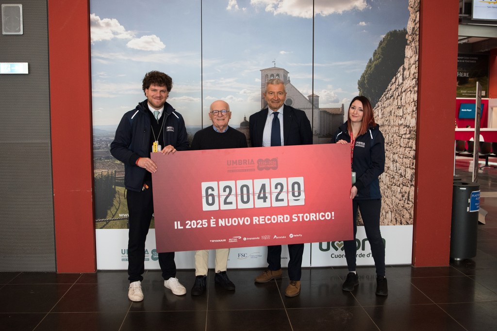 Quattro persone sorridenti in un aeroporto tengono un cartello che celebra il record di 620.420 passeggeri nel 2025.