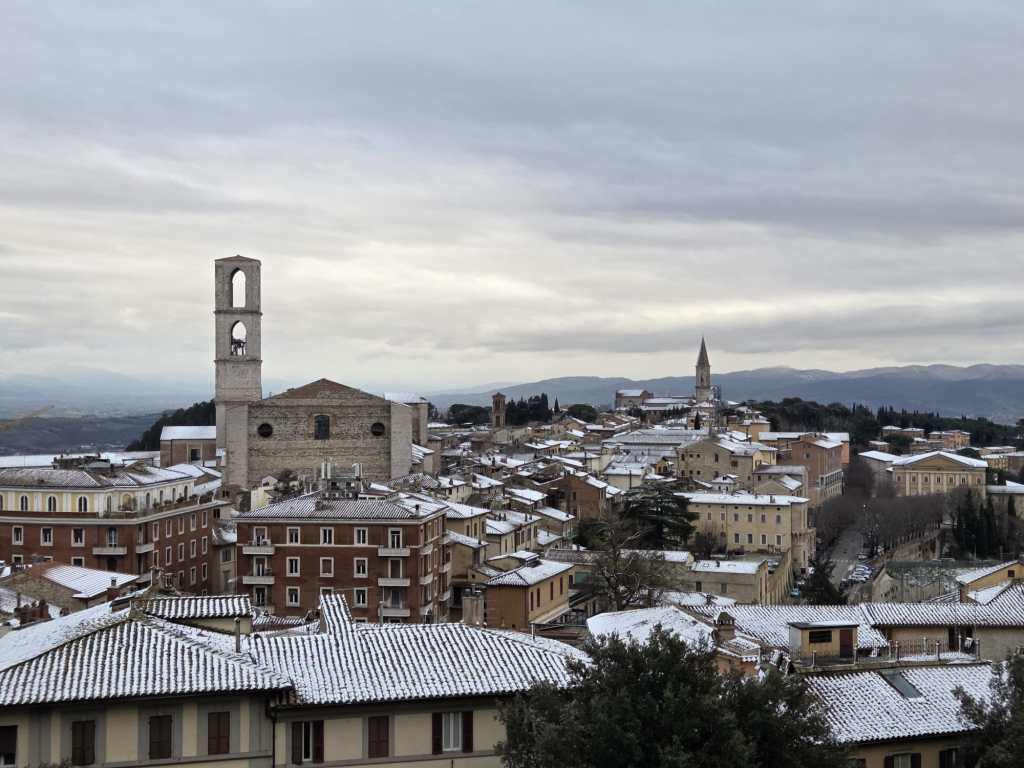 Panorama di Perugia con tetti coperti di neve sotto un cielo nuvoloso.