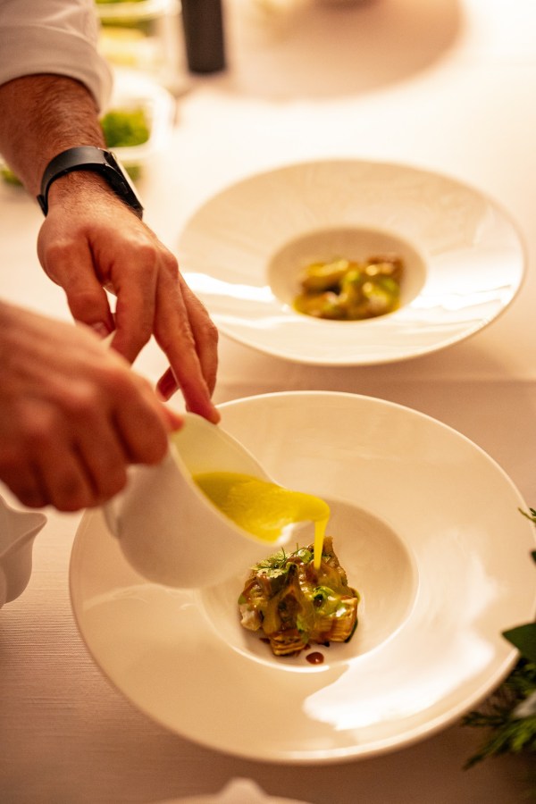 A chef pouring sauce over a plated dish in a fine dining setting, highlighting the intricate presentation of the food.