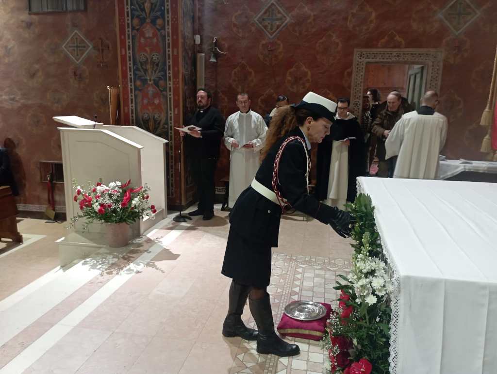 A woman in formal attire adjusts floral decorations on an altar in a church during a ceremony. Several attendees, including individuals in religious garments, are present in the background.