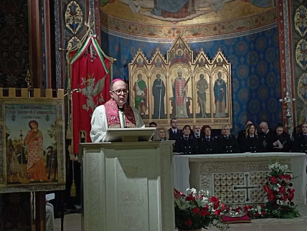 A clergy member in formal attire delivers a speech at a religious ceremony, with an ornate altar and colorful frescoes in the background. Attendees in uniform are seated behind him, and there are religious banners and a decorative altar in the scene.