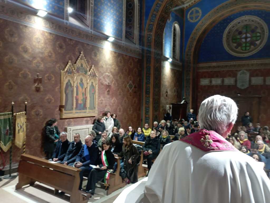 A view from behind a speaker in religious attire, facing a congregation seated in a beautifully decorated church with a painted ceiling and large wall artwork.