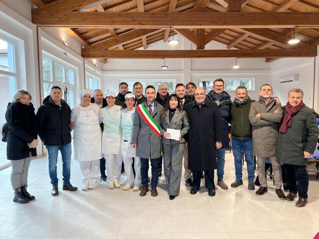 Gruppo di persone in un ambiente interno luminoso, con decorazioni in legno e un'atmosfera conviviale, durante la visita istituzionale della Presidente della Regione Umbria.