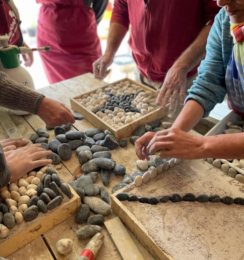 Group of hands arranging various stones on a wooden table, with some stones placed in trays.