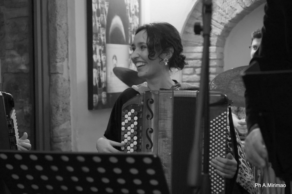 A woman playing an accordion with a joyful expression in a music performance setting.
