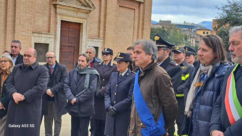A group of people, including officials in formal attire, gather outdoors near a building, some wearing uniforms and ceremonial sashes, during an event.