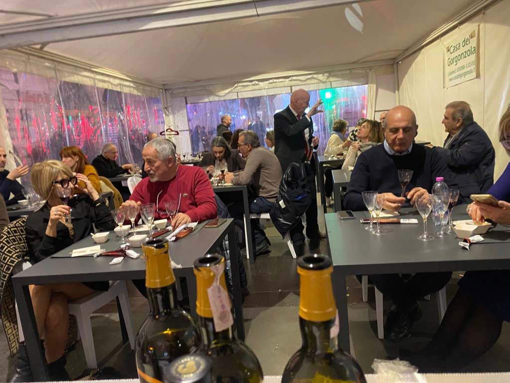 A lively dining scene inside a tented area with people seated at tables enjoying drinks and conversing.