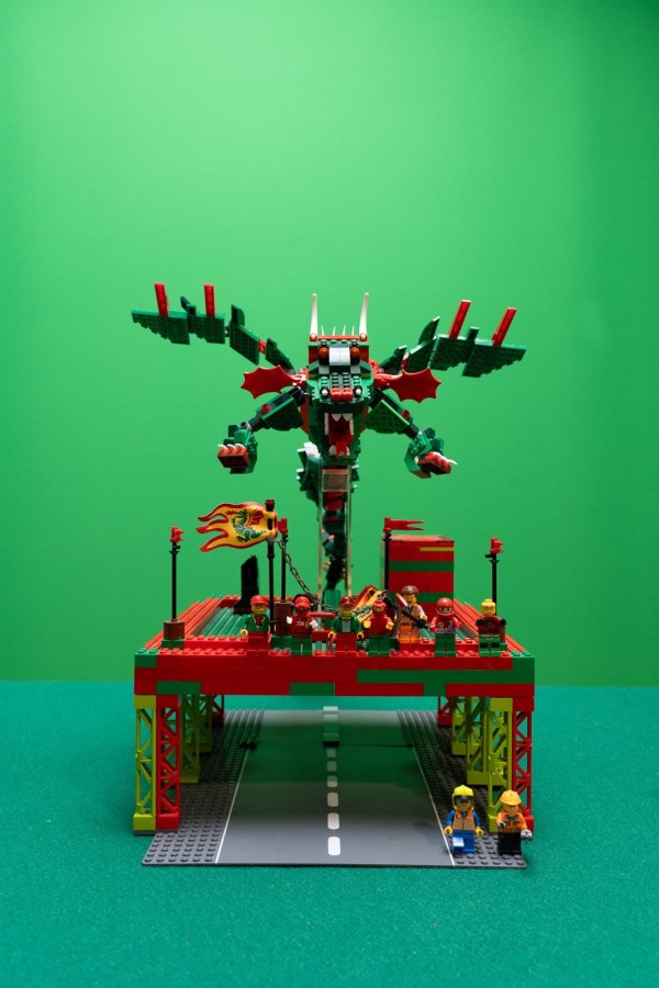 A colorful LEGO dragon towering over a construction-themed scene with minifigures on a platform, set against a green background.