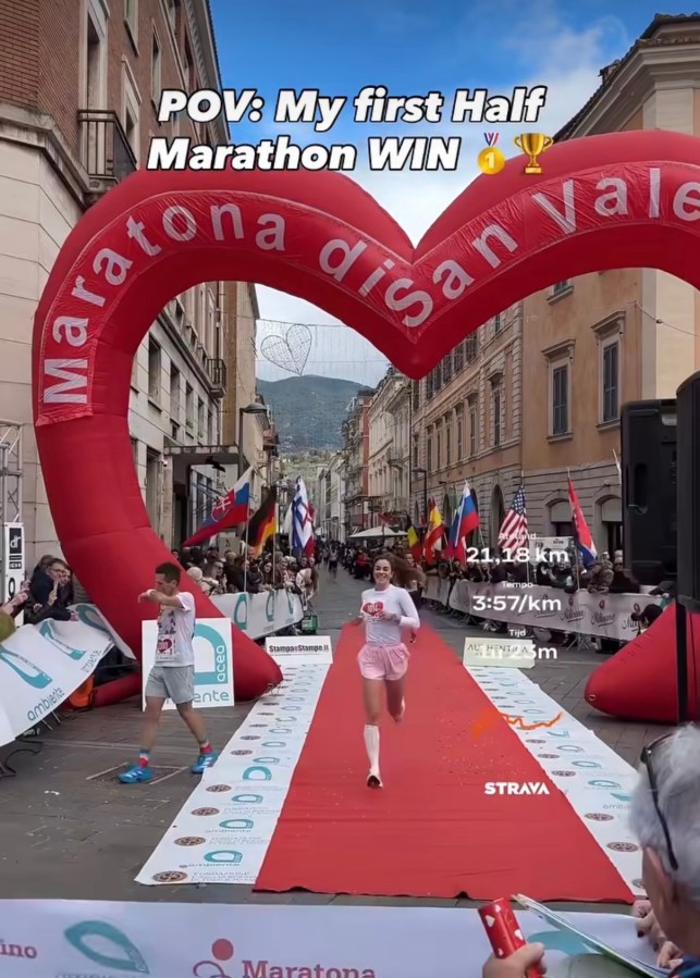 Runner crossing the finish line at a half marathon event, under a heart-shaped arch with flags in the background.