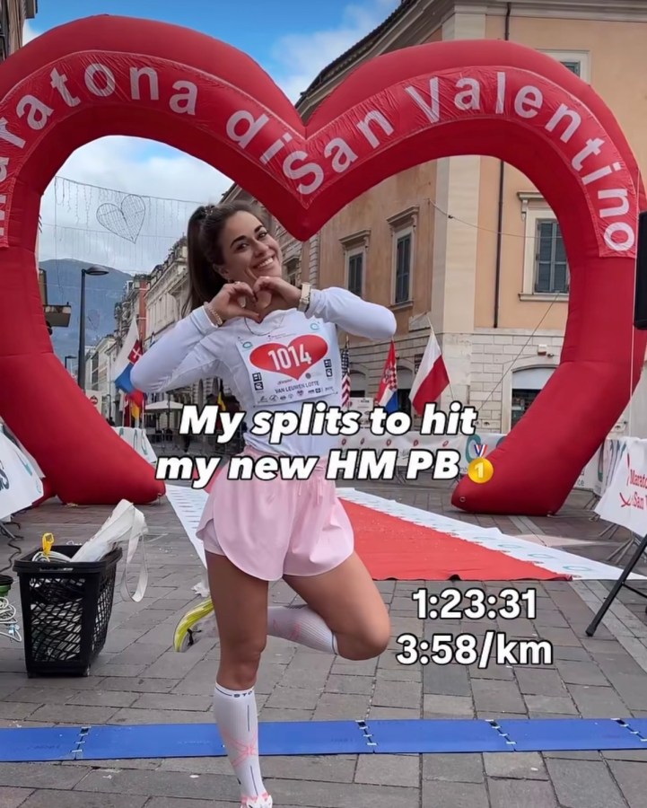 A runner poses with a heart-shaped inflatable arch in the background, celebrating her new half marathon personal best time of 1:23:31, with splits of 3:58/km. She is wearing a race bib number 1014 and making a heart gesture with her hands.
