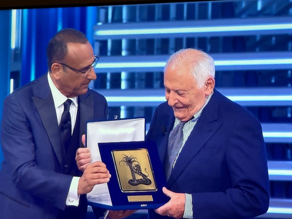 A man in a suit presenting an award to an older gentleman holding a plaque, both smiling during a ceremony.
