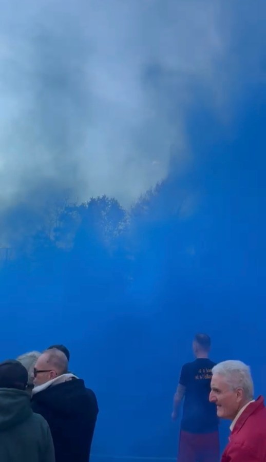 A crowd of people standing amidst blue smoke in an outdoor setting.
