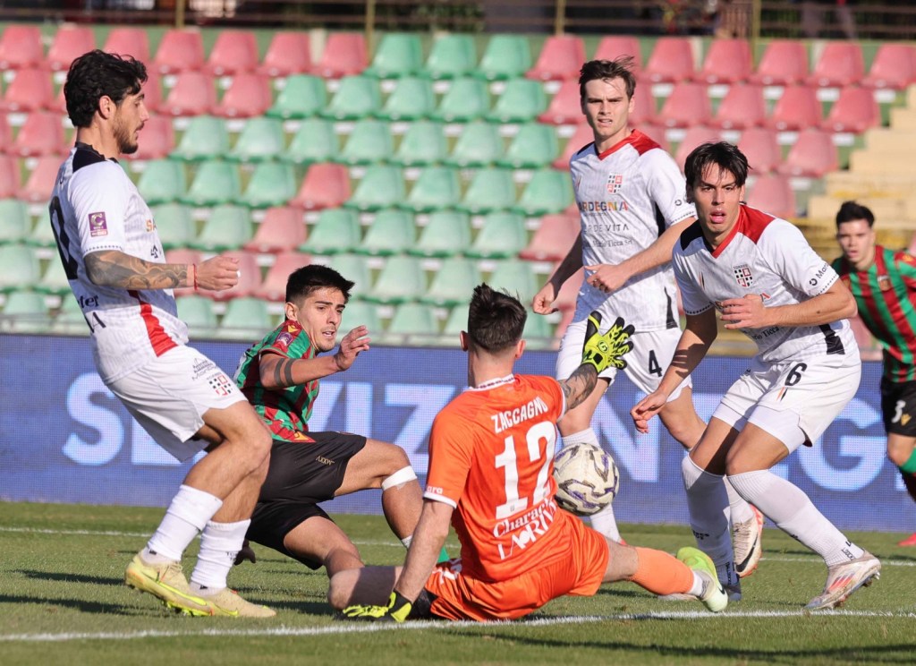 A soccer game scene featuring players in action, with two teams competing on the field. A goalkeeper in orange is attempting to secure the ball while a player in striped attire challenges him. Other players are positioned nearby, showcasing dynamic movements during the match.
