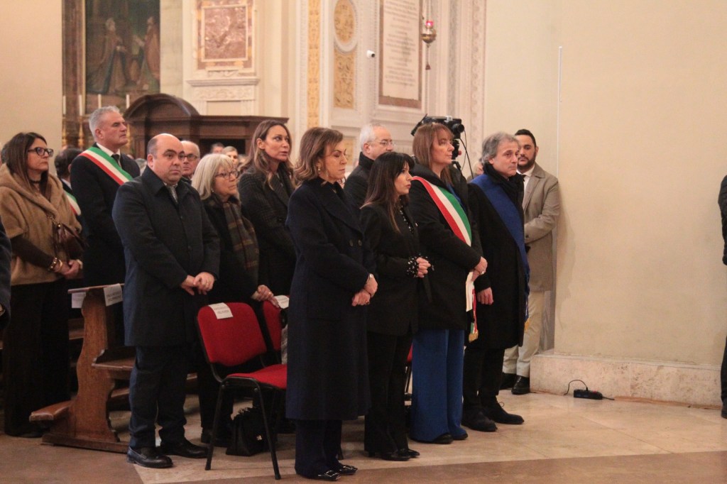 A group of people standing in a formal setting, possibly during a ceremony, with some individuals wearing sashes and formal attire.