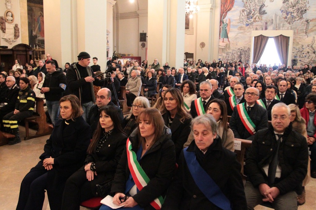 A large crowd seated in a church, including various officials wearing sashes, during a formal event.