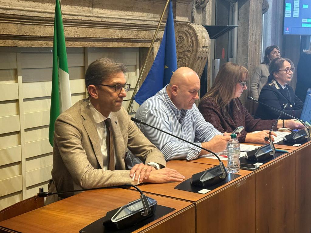 A group of people seated at a conference table with flags in the background, engaged in a discussion or meeting.